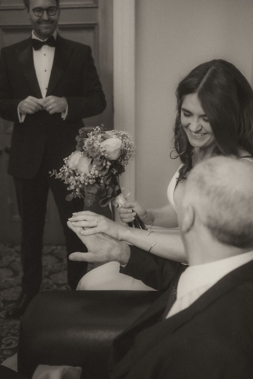 A black and white wedding photo showing a couple and guests in formal attire with a lovely floral bouquet.