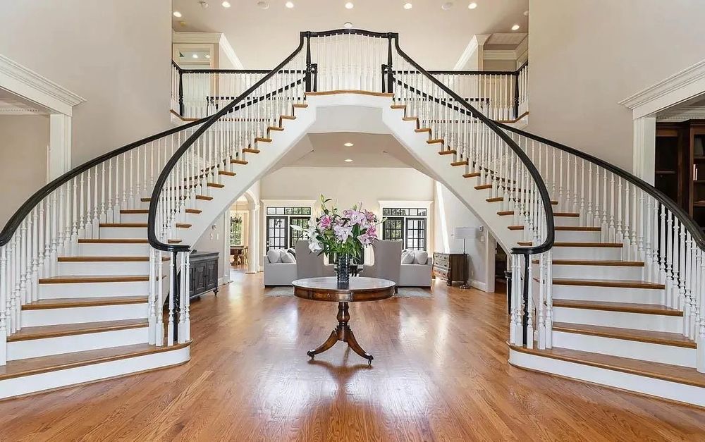 Grand foyer with symmetrical curved double staircases and hardwood floors leading to an elegant center table.