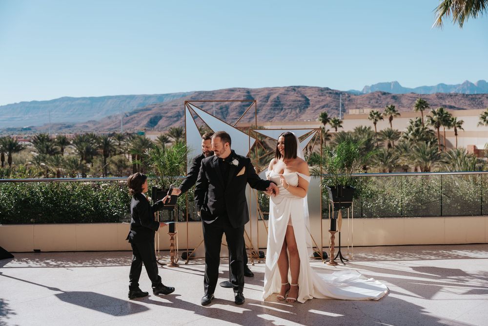 An outdoor wedding ceremony takes place on a sunny terrace with scenic desert mountains and palm trees in the background.