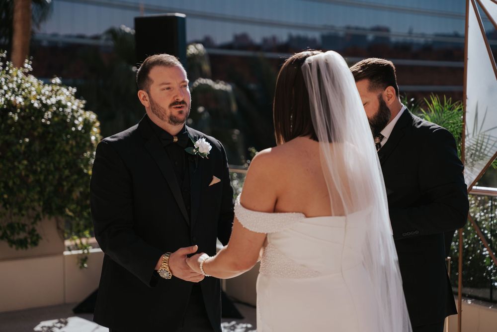 A happy couple shares a moment during their wedding ceremony on a sunny outdoor terrace.