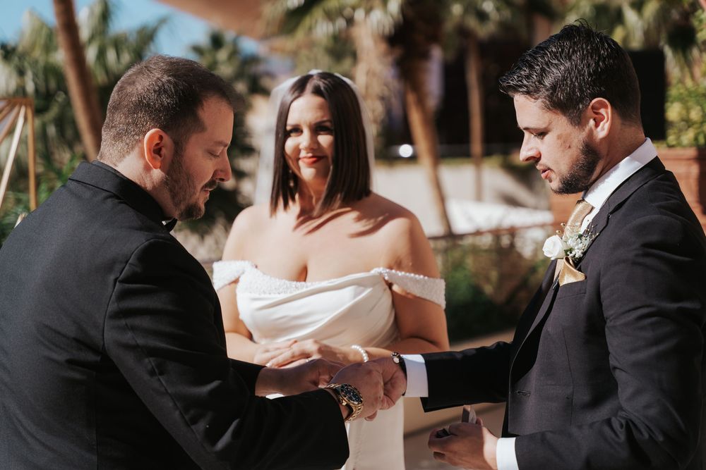 Two people exchanging vows during an outdoor wedding ceremony on a sunny day, surrounded by nature.