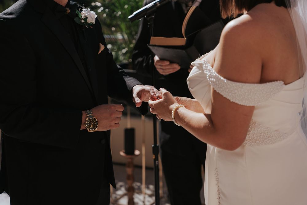 Exchange of rings during an outdoor wedding ceremony between couple in formal attire.