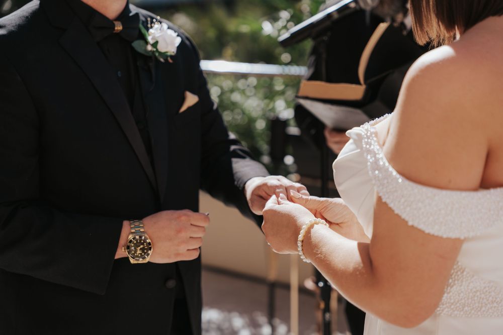 Wedding couple exchanging rings during an outdoor ceremony with hands in focus.