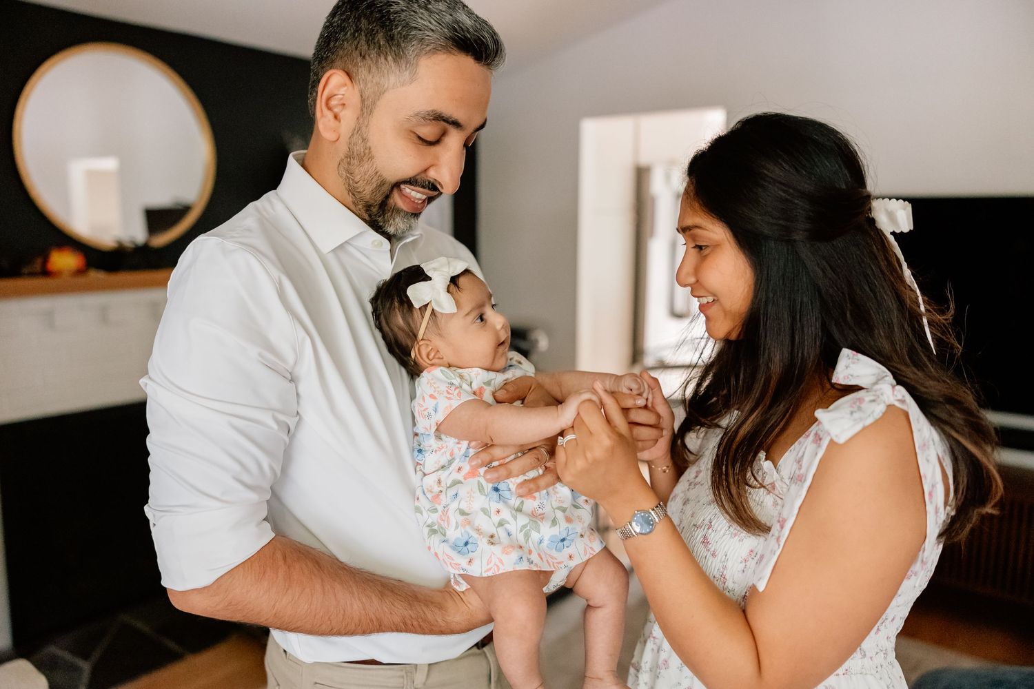 A happy couple sharing a tender moment while holding their newborn baby in their living room.