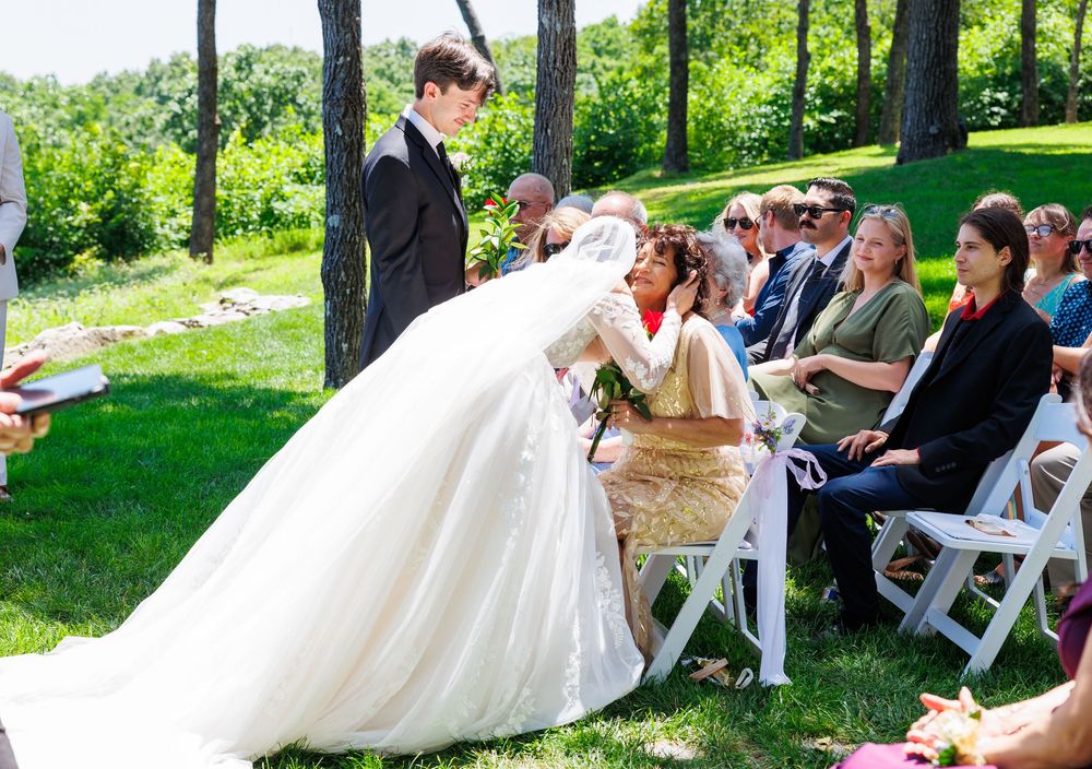 Outdoor wedding ceremony on a sunny day with white chairs arranged on a grassy lawn capturing candid guest moments.