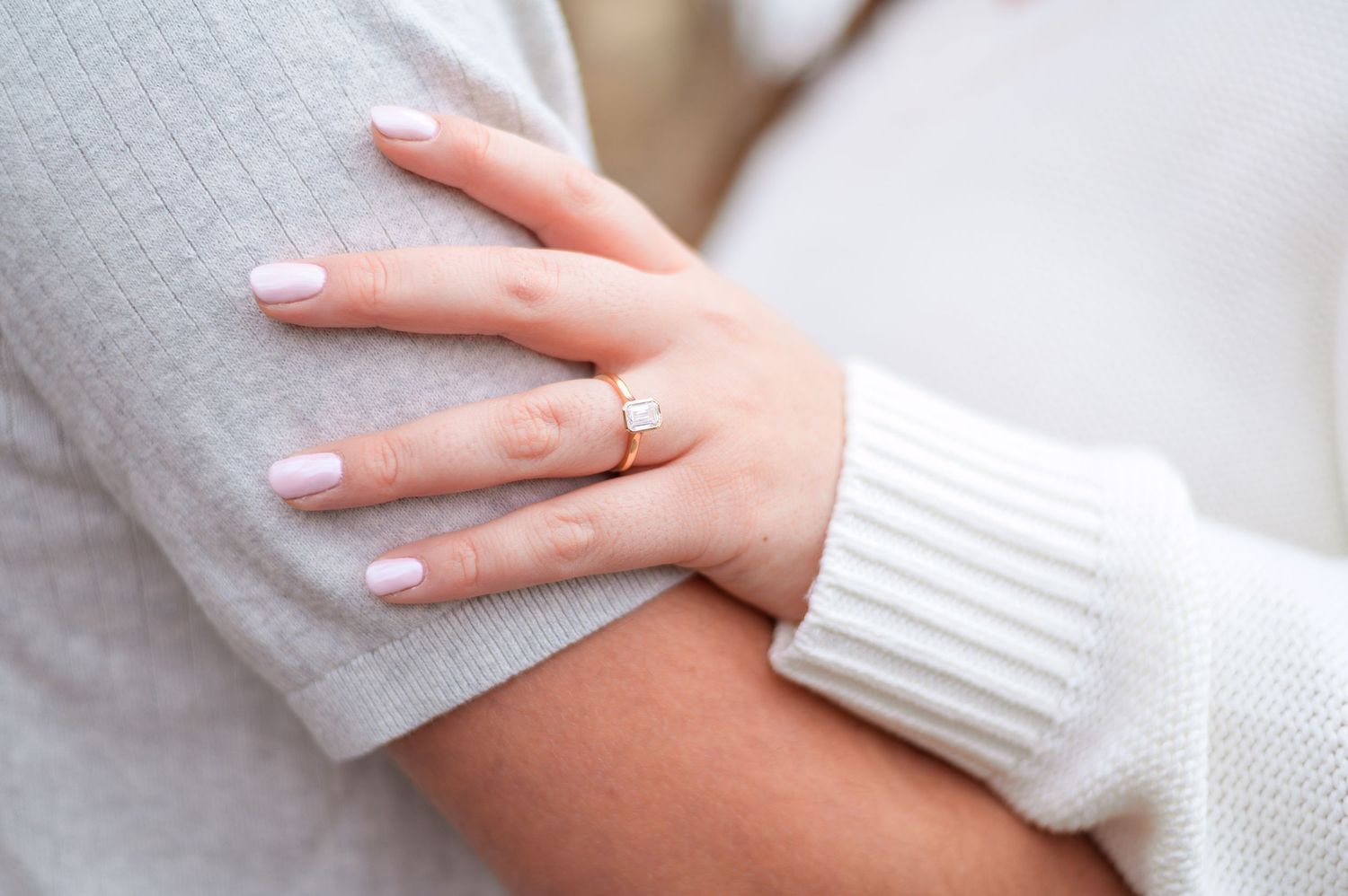 Close-up of a hand with an engagement ring resting on a white sweater sleeve.