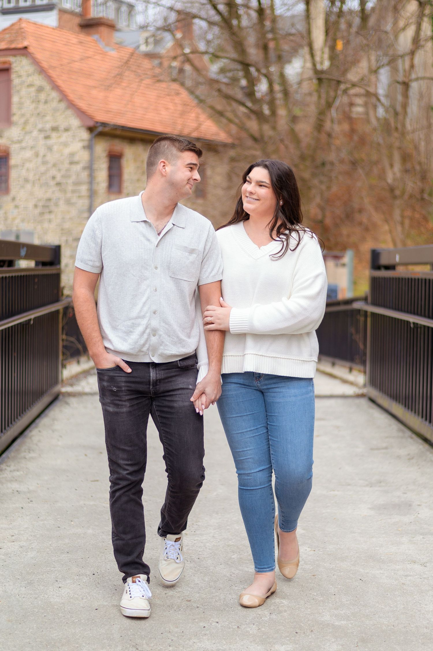 A couple walking together on a bridge near a rustic stone building.