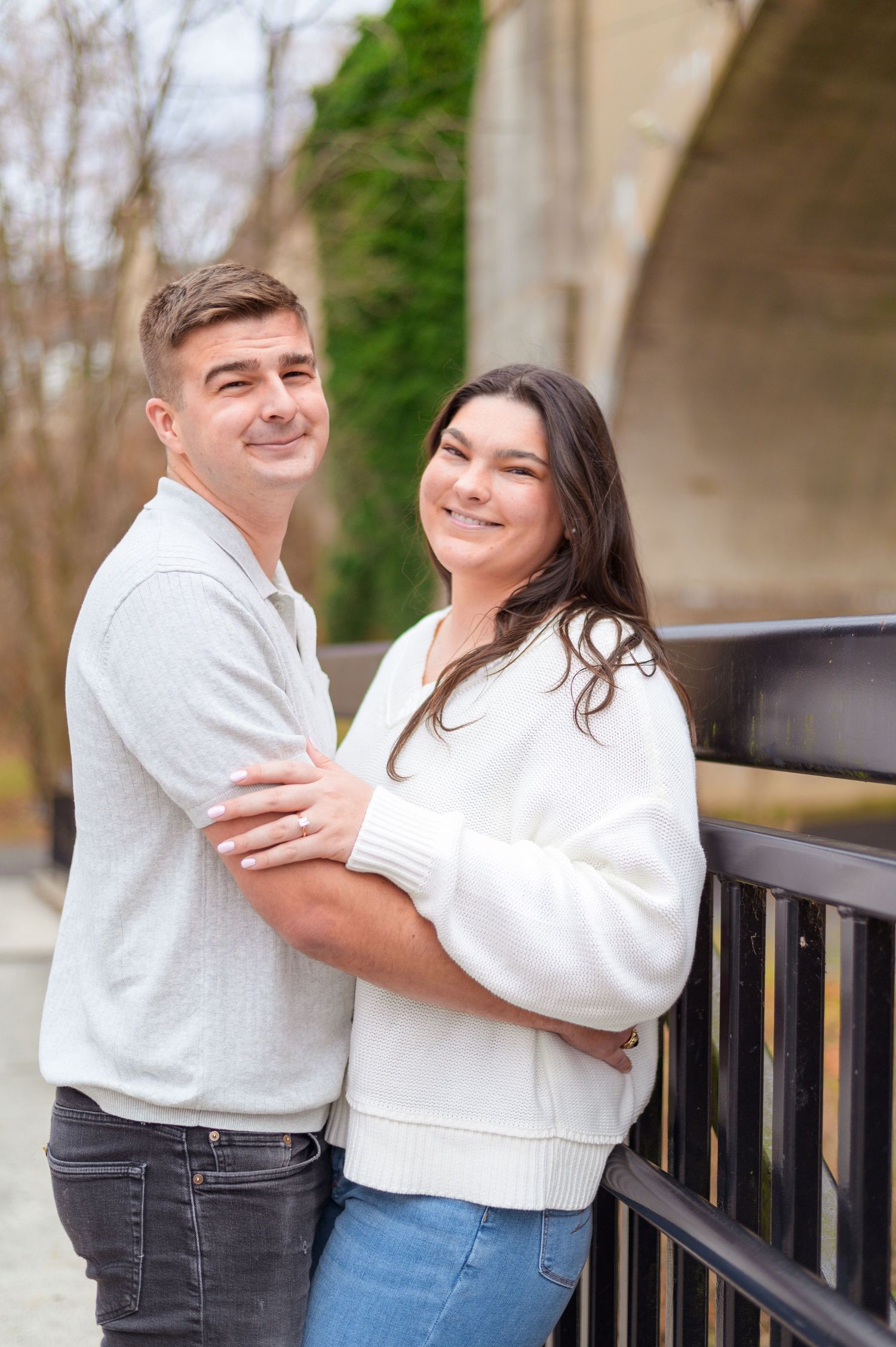A couple embracing and smiling while standing by a railing outdoors.