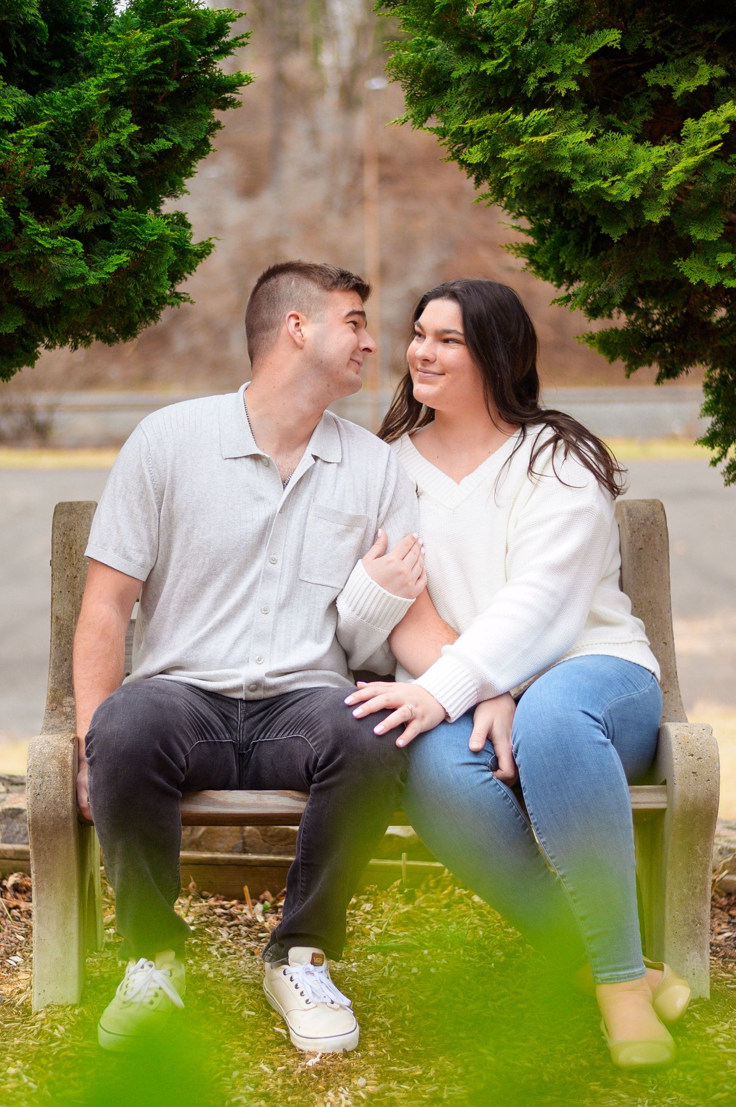 Couple sitting close together on a bench surrounded by evergreen trees.