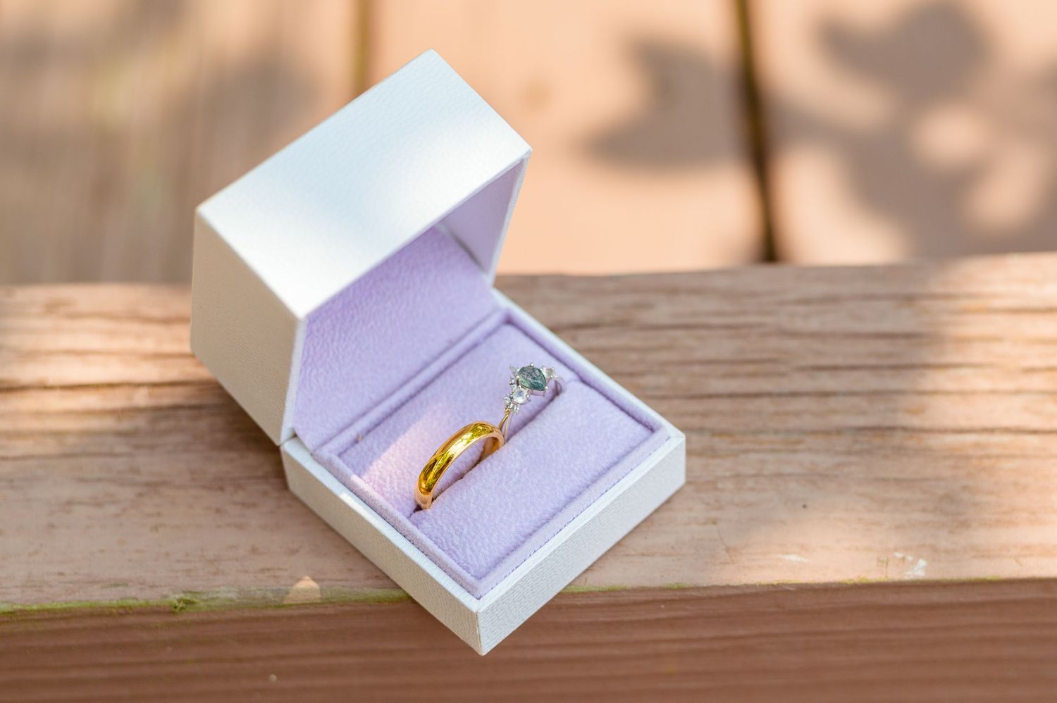 An engagement ring displayed in a white jewelry box with purple interior.