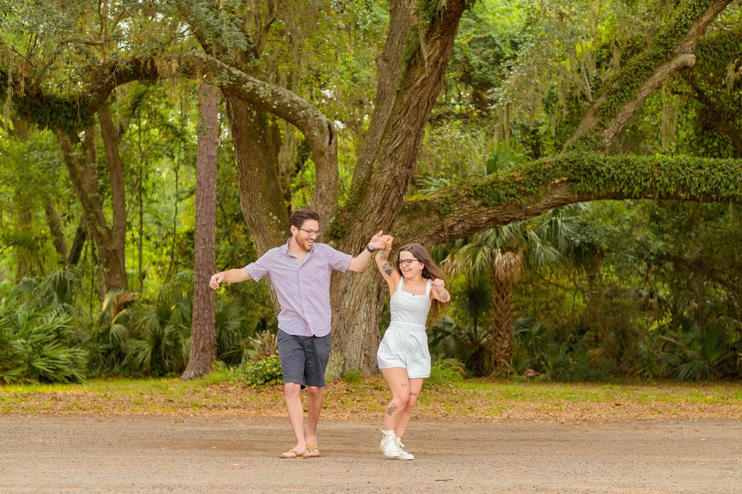 A couple runs joyfully through a lush green forest path.
