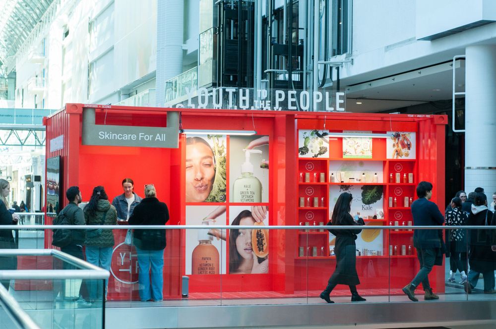 A modern red retail pop-up store with glass displays attracts customers on a busy shopping street.