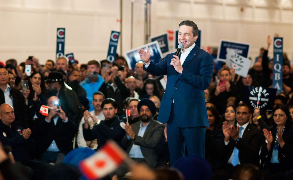 Enthusiastic speaker addresses large crowd at political rally with supporters holding campaign signs in background.