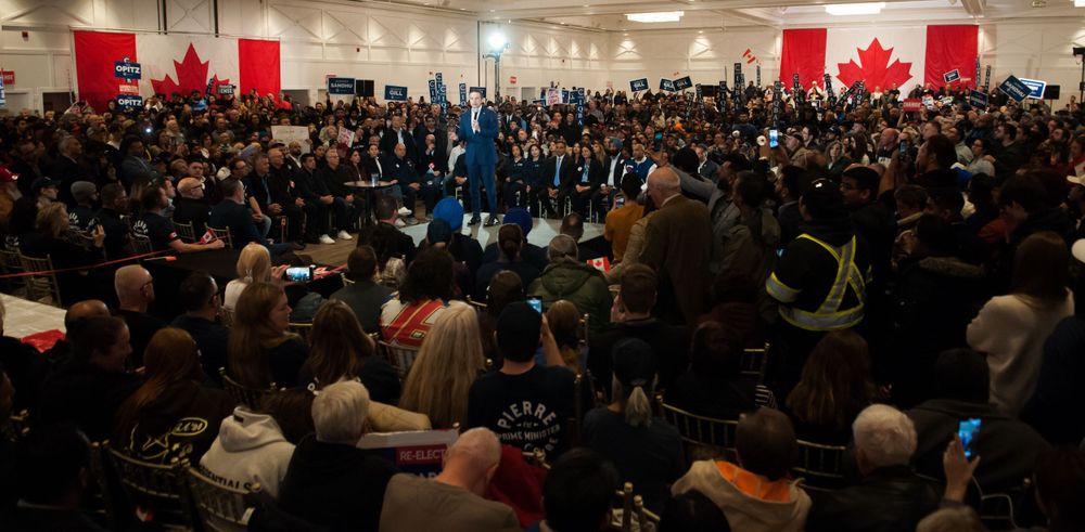 A large crowd gathered in an auditorium with Canadian flags displayed prominently on the wall during a ceremony.