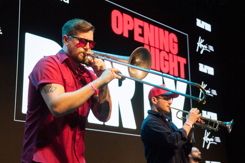 Two musicians play trumpets on stage with an 'Opening Night' sign illuminated behind them.
