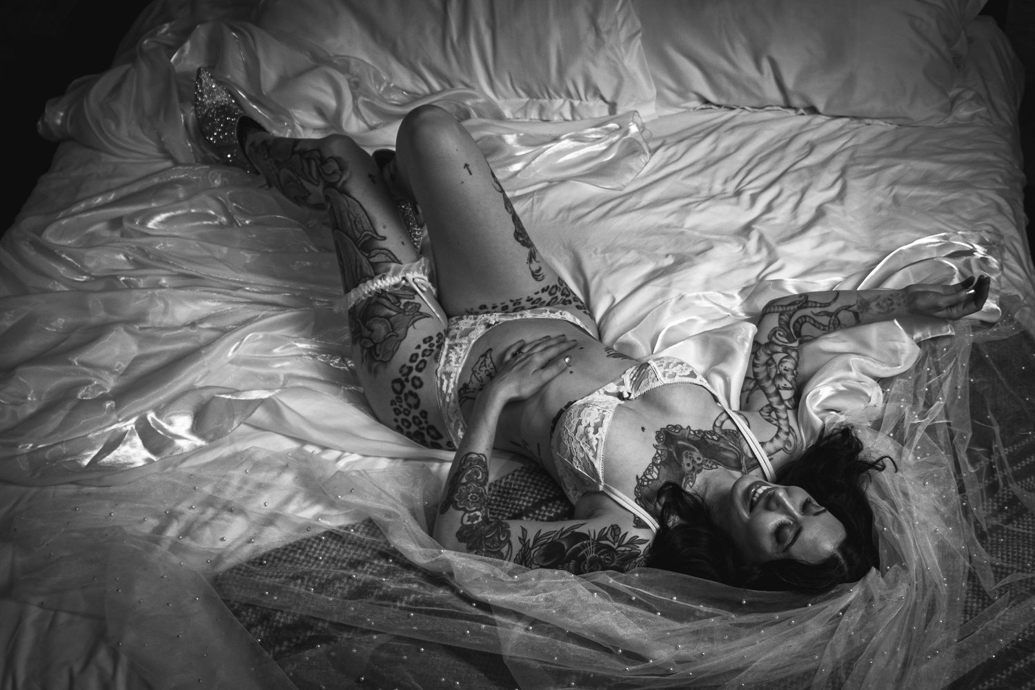 Artistic black and white boudoir photo of person lying on textured bedding.