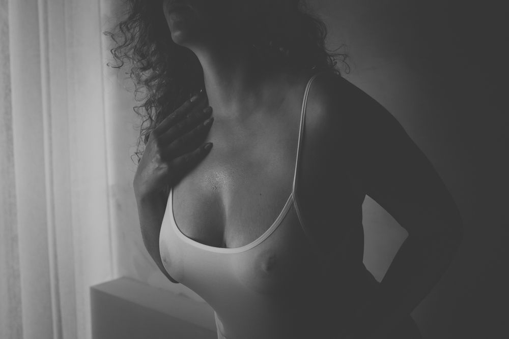 Black and white artistic boudoir photo of a silhouette figure in white lingerie near a window.