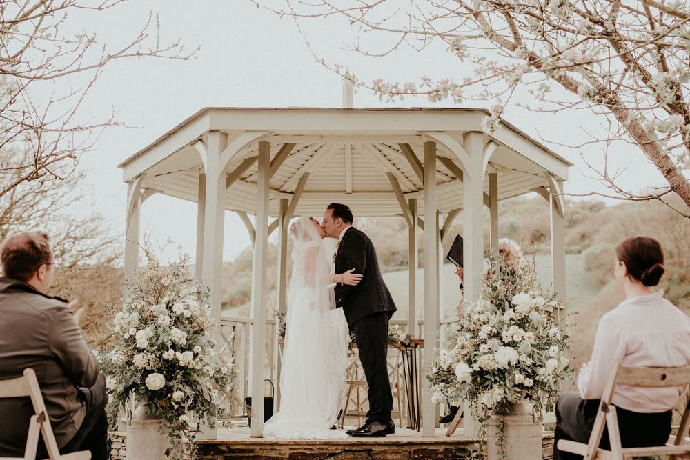 White garden gazebo decorated with floral arrangements hosts an intimate outdoor wedding ceremony on a winter day.