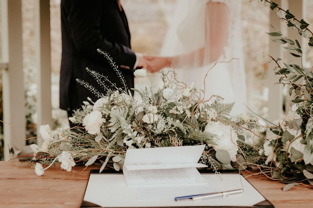 Wedding ceremony details with an elegant floral arrangement and guestbook signing setup on a wooden table.