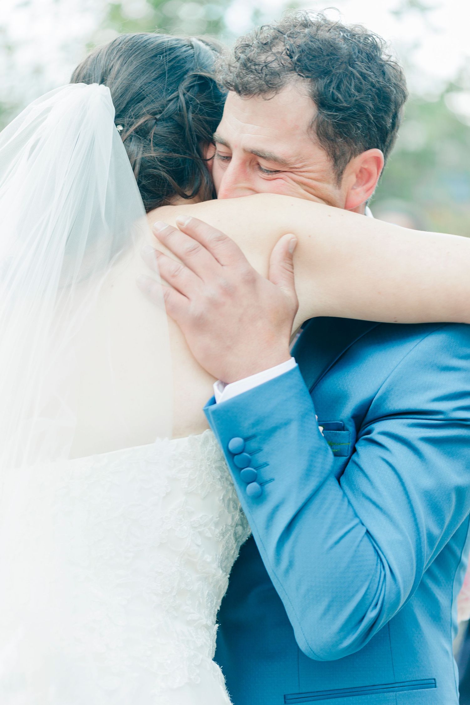 Emotional embrace between newlyweds at outdoor wedding ceremony with soft natural lighting.