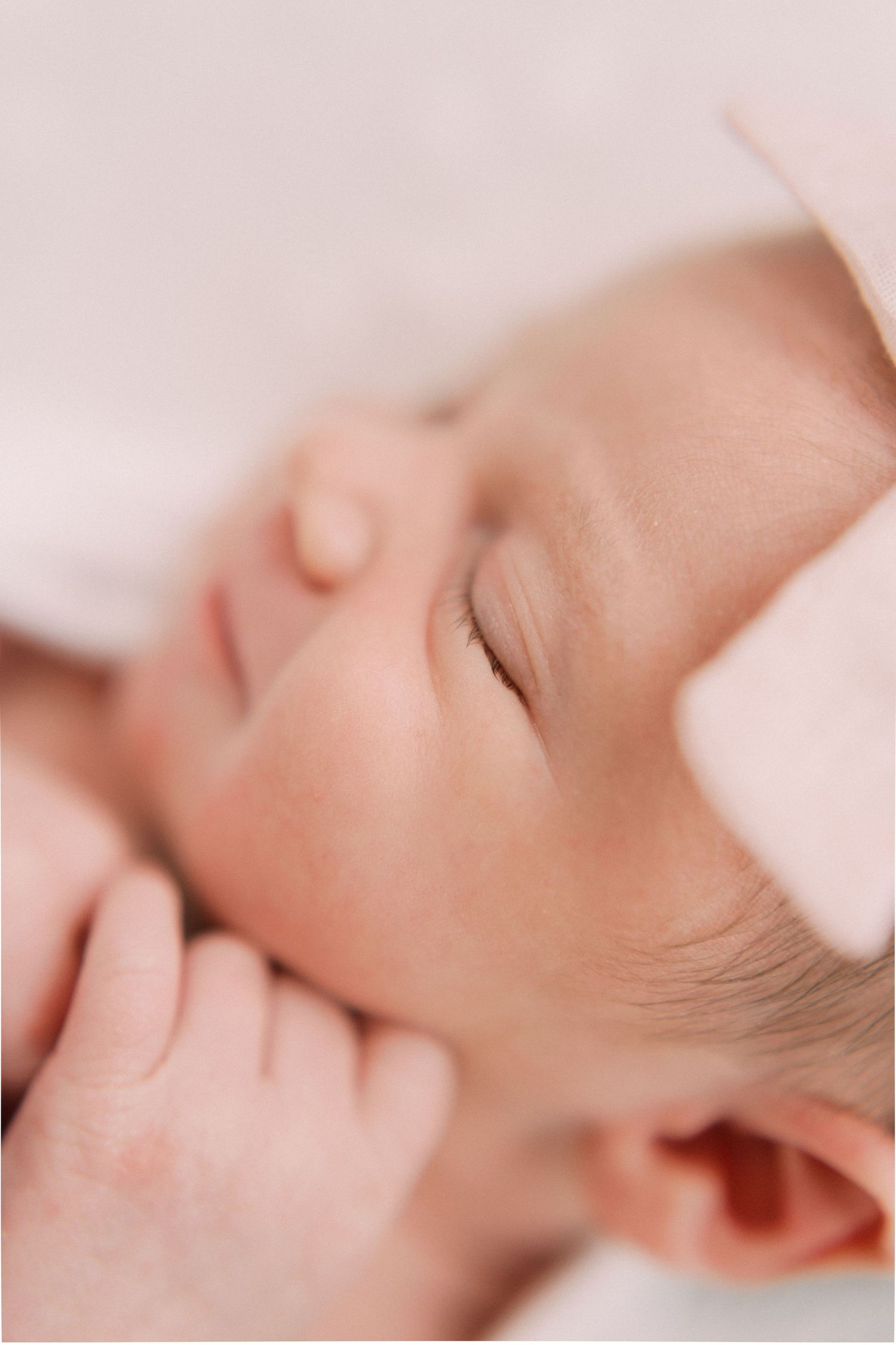 A sleeping baby rests peacefully against soft pink linens in a delicate close-up photo.
