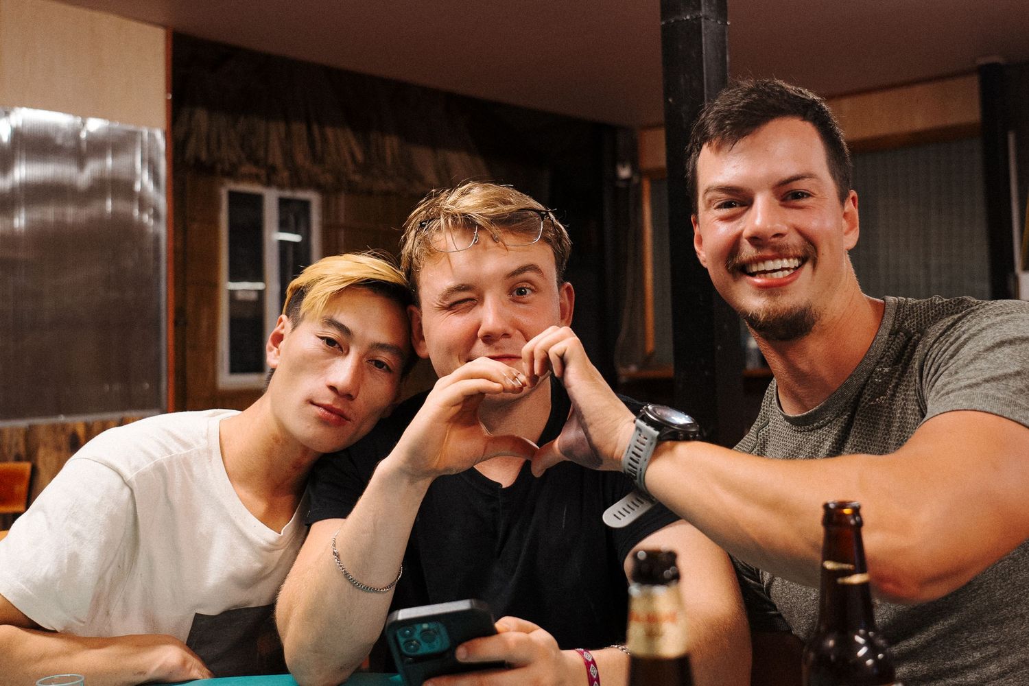 Three friends relaxing and having drinks together at a pub counter in warm lighting.