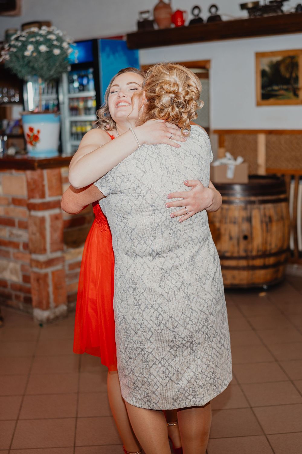 Two people share a joyful embrace at a rustic venue with brick walls and wooden barrel decor.