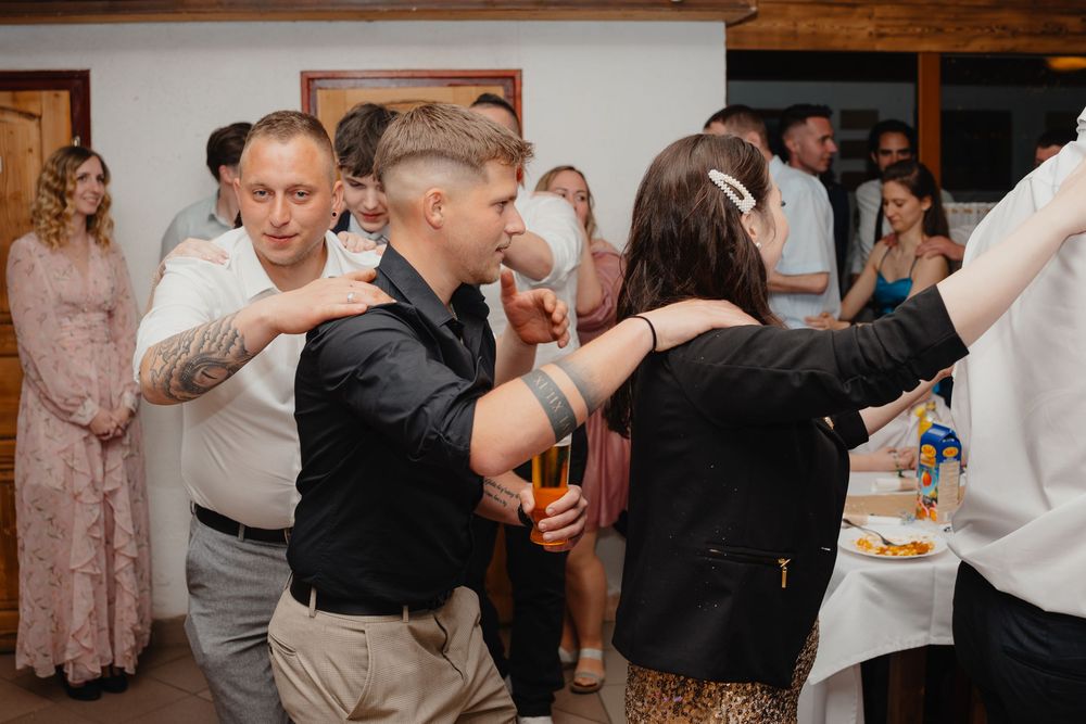 Wedding guests dance and celebrate together at an indoor reception venue with rustic wooden beams and decor.
