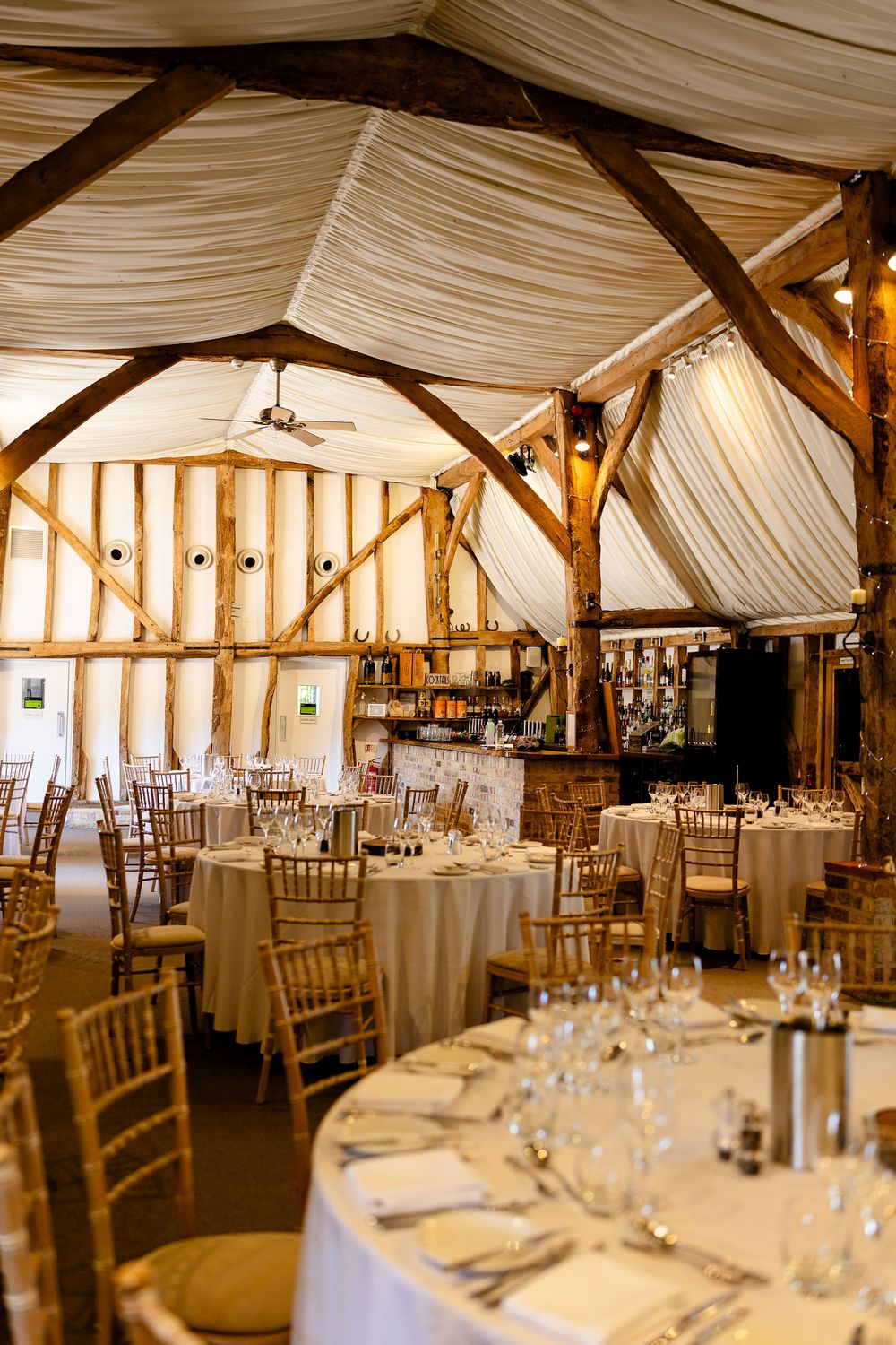 Elegant barn wedding venue with draped fabric ceiling, wooden beams, and round tables set for reception.