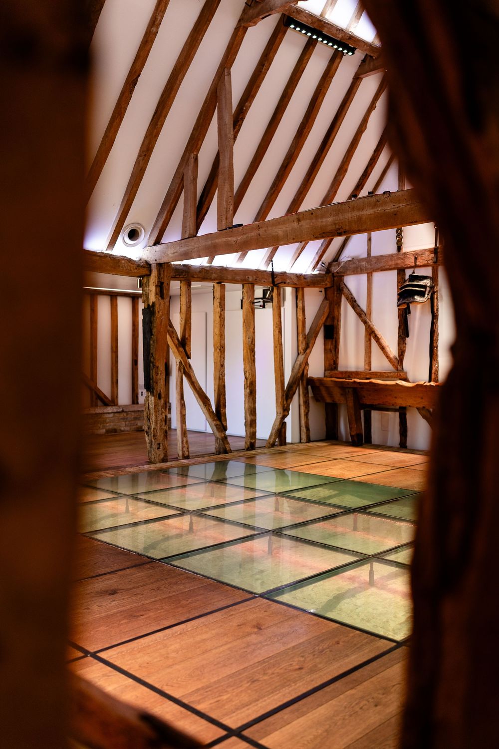 Interior view of a rustic timber-framed room with wooden beams and a geometric patterned floor.