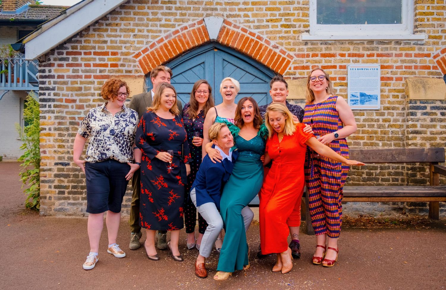 Cheerful wedding group laugh and strike a fun pose in front of a blue door on a brick building.