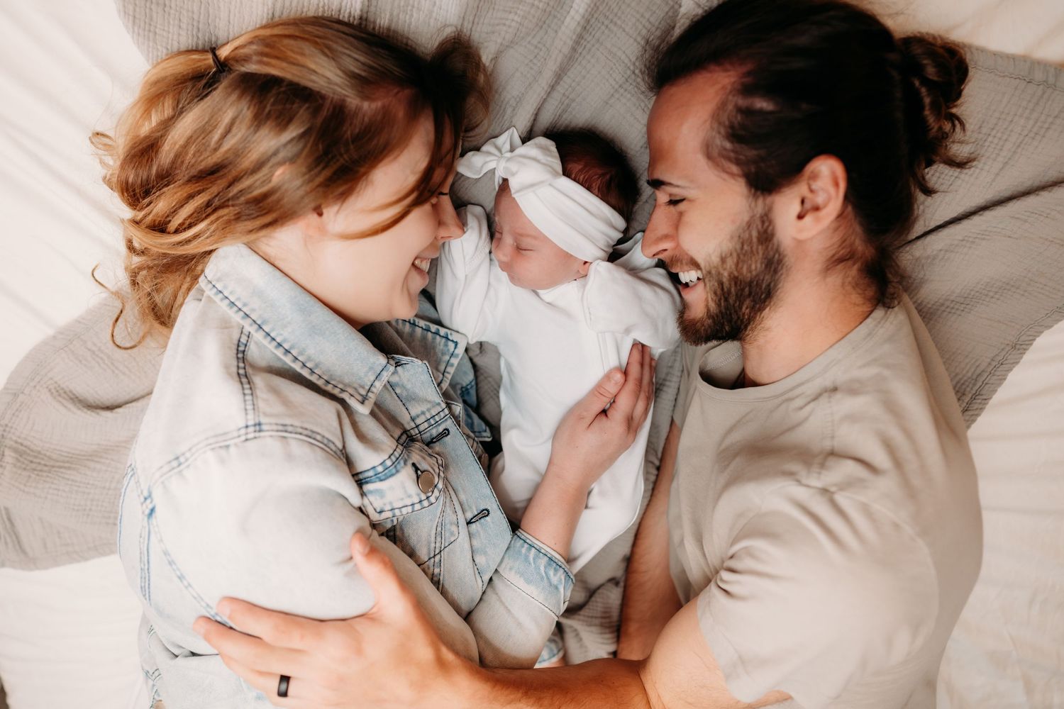 Happy family with newborn baby snuggling together on white bedding in intimate lifestyle moment.