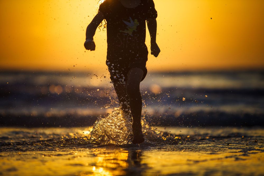 Silhouette of runner splashing through shallow water on beach at golden sunset.