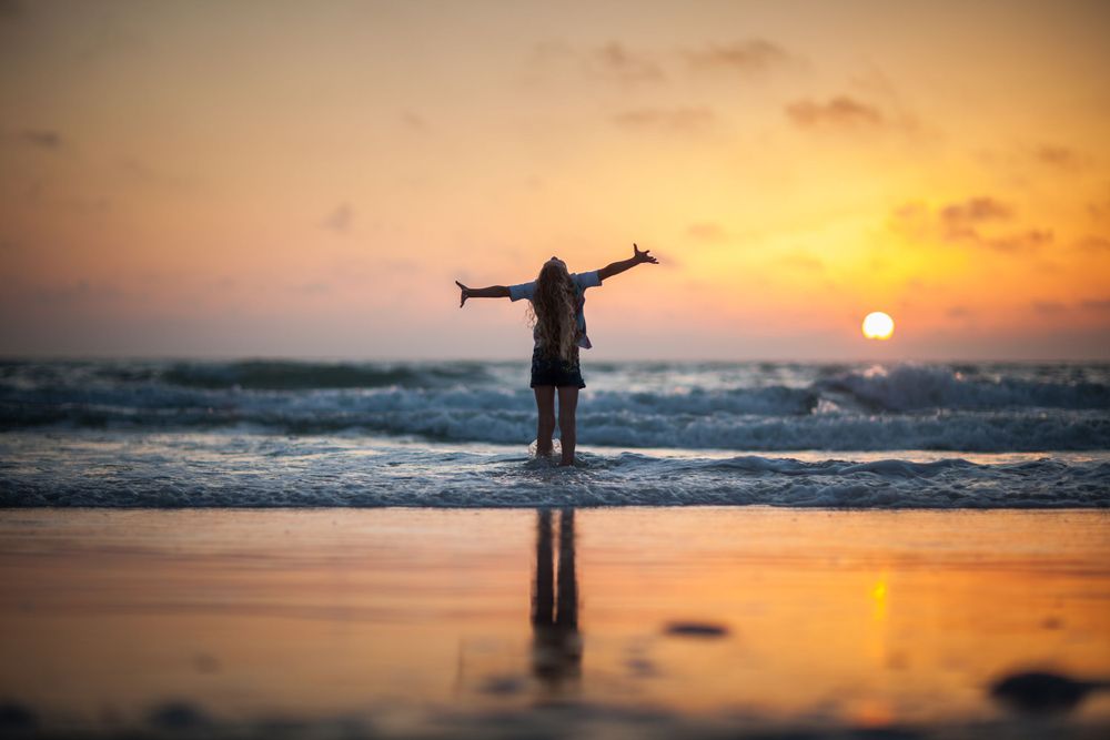 Silhouette of person with raised arms against dramatic orange beach sunset.