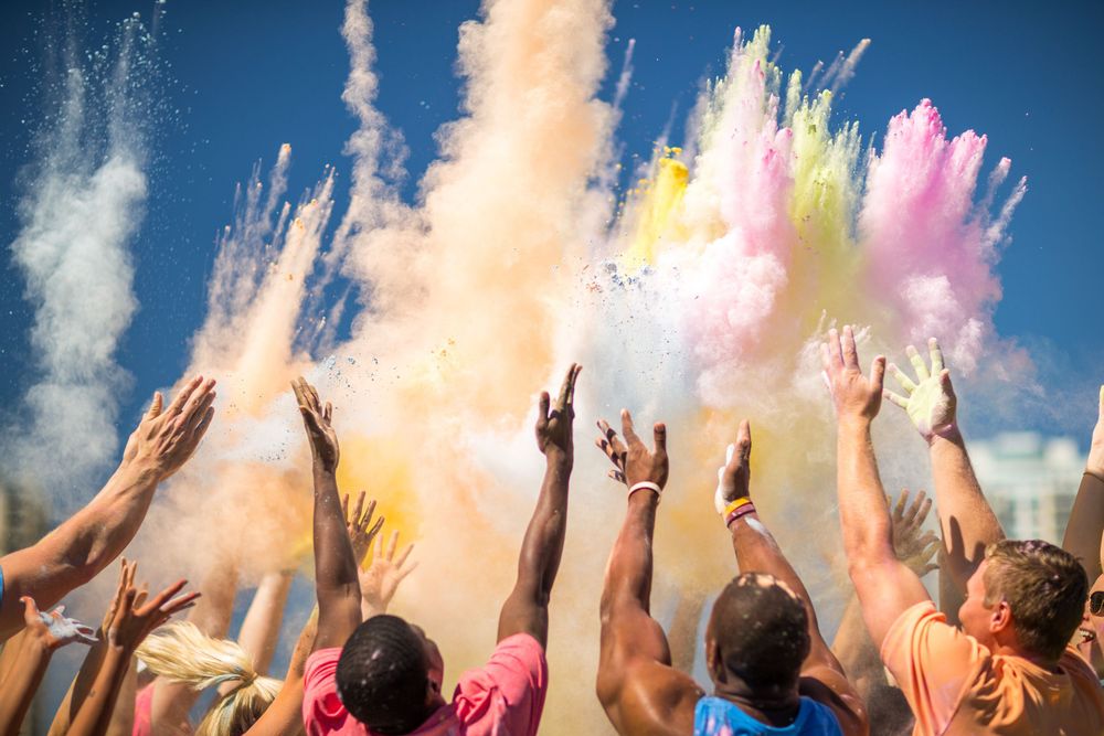 People throwing colorful powder into the air at an outdoor festival against a bright blue sky.