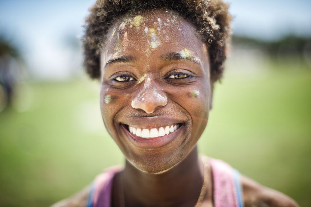 Close up portrait of a smiling person with bright teeth and natural hair against a blurred green background.