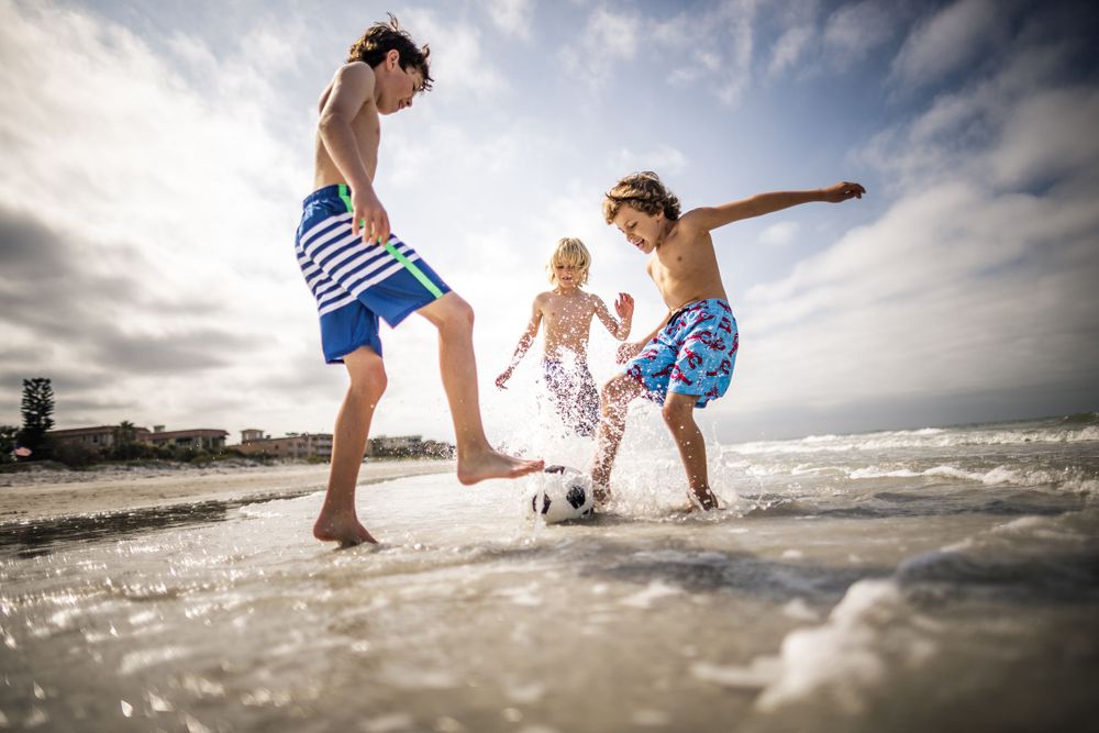 Three people splashing and playing in the shallow ocean waves during sunset on a beach.