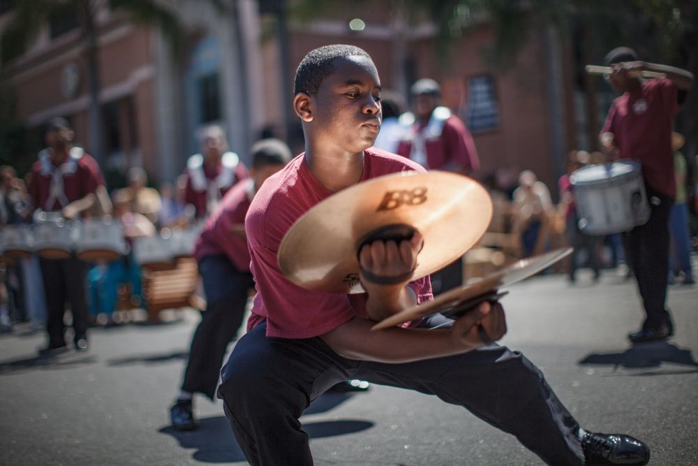 A street performer crouches while skillfully balancing cymbals during a vibrant outdoor performance.