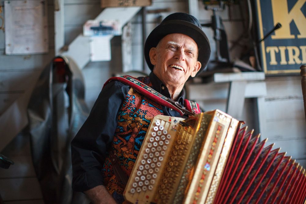 A cheerful musician in a black hat plays a decorative red accordion while smiling warmly.