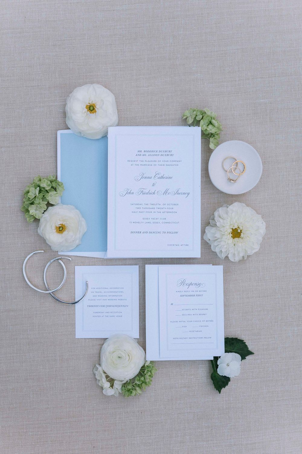 Elegant wedding invitation suite with white flowers and rings on linen background.