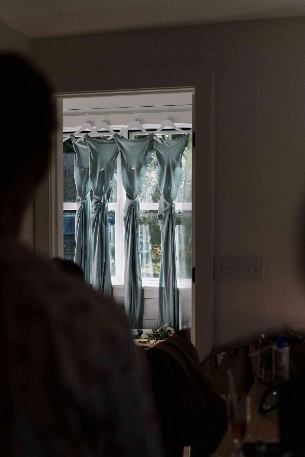 Row of sage green bridesmaid dresses hanging in a room.