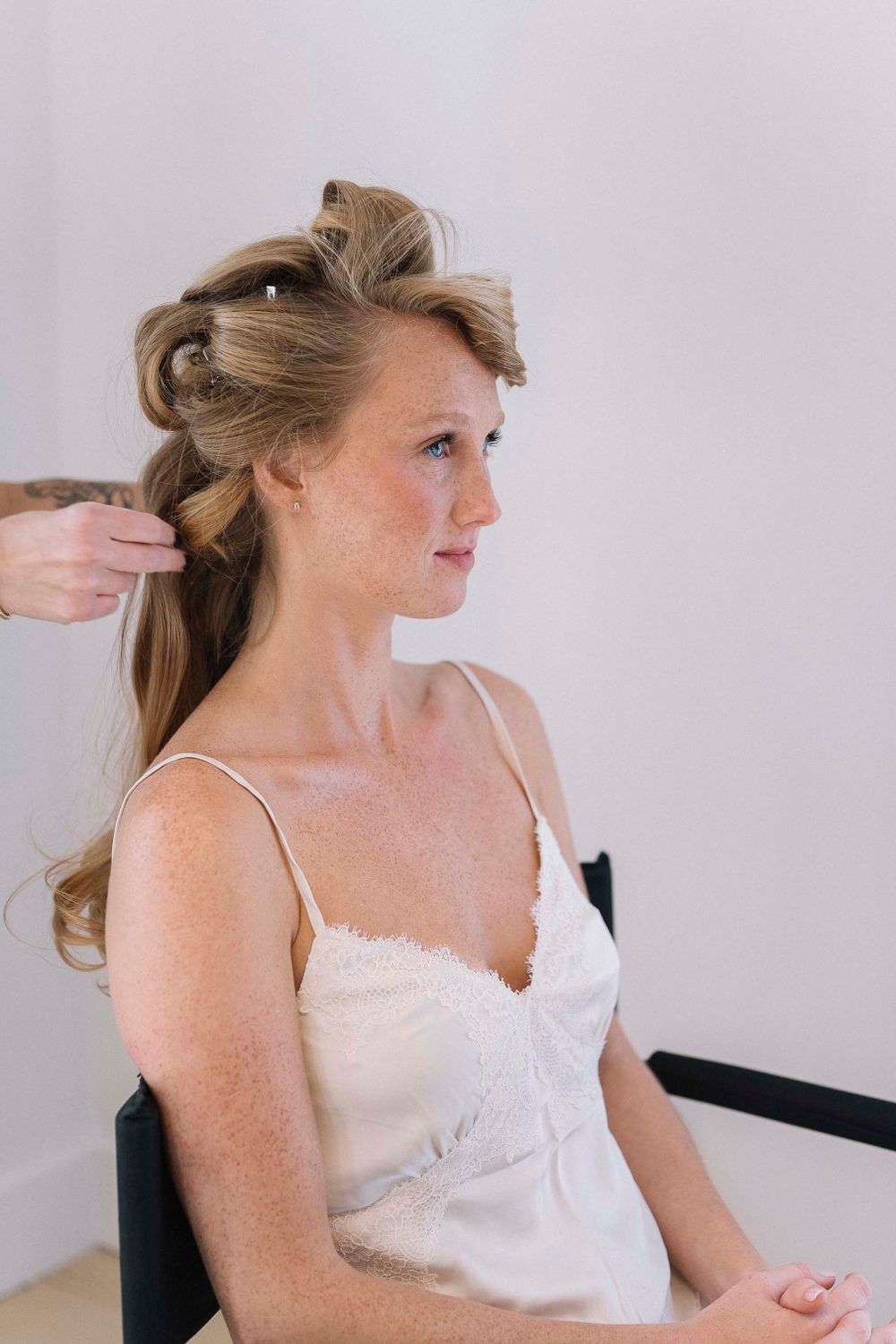 A bride gets her hair styled while sitting in a white robe.