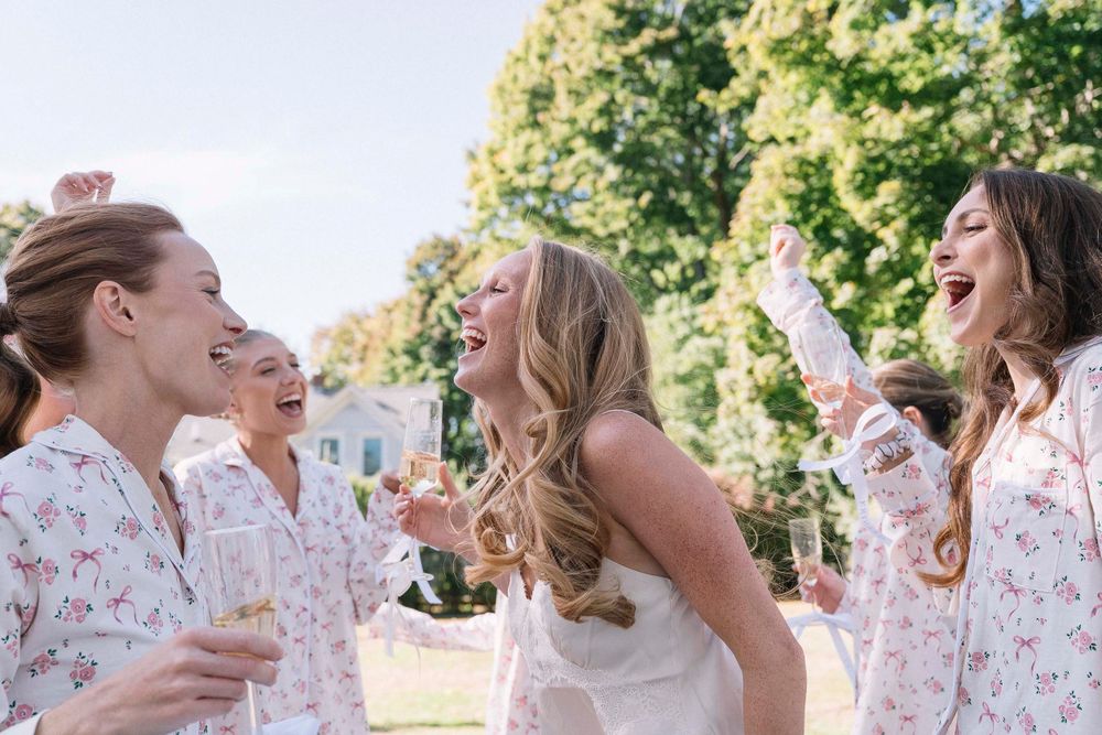 Wedding party guests share joyful laughter while holding champagne glasses at an outdoor celebration.
