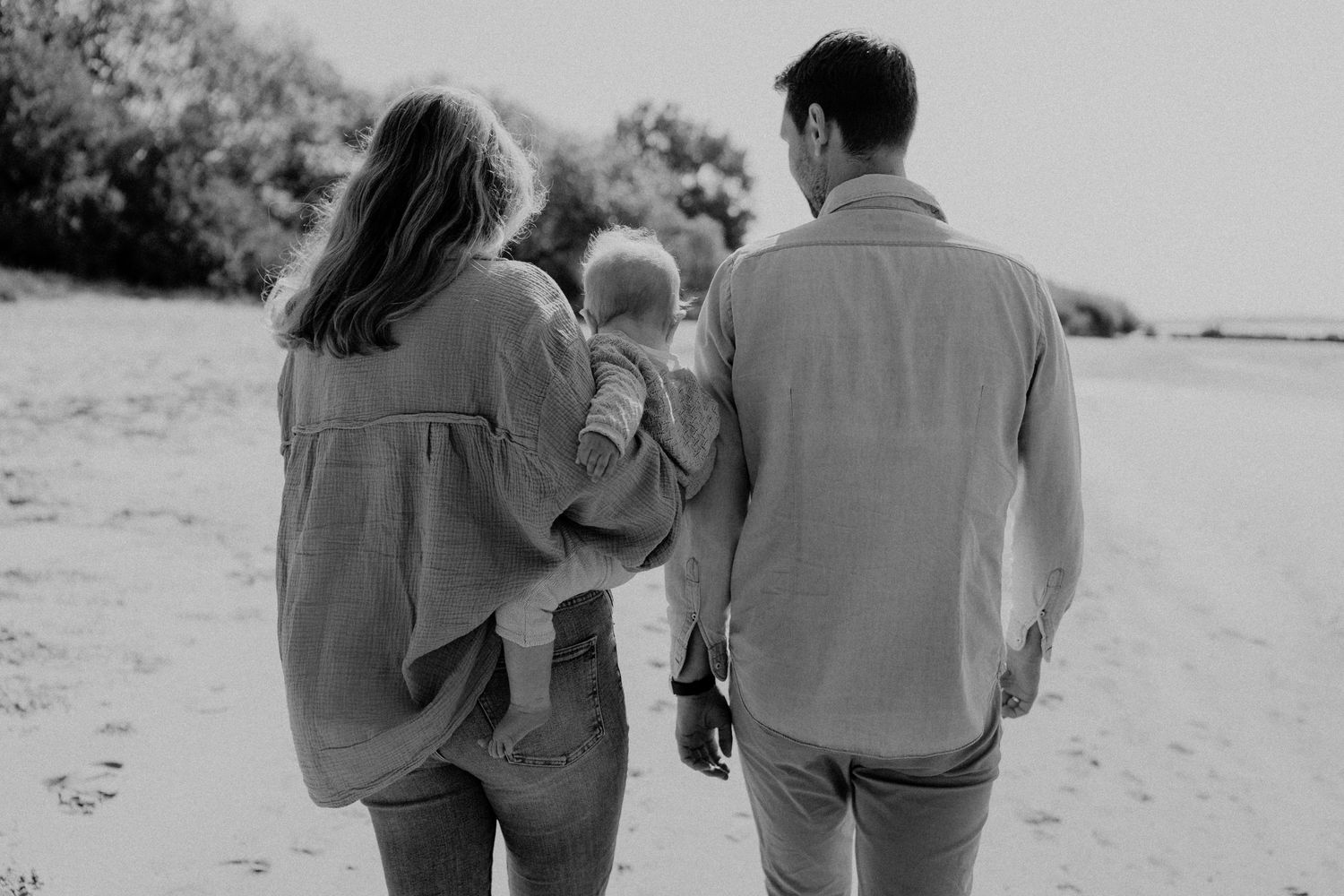 Black and white photo of family walking together on path with parents and baby held between them.