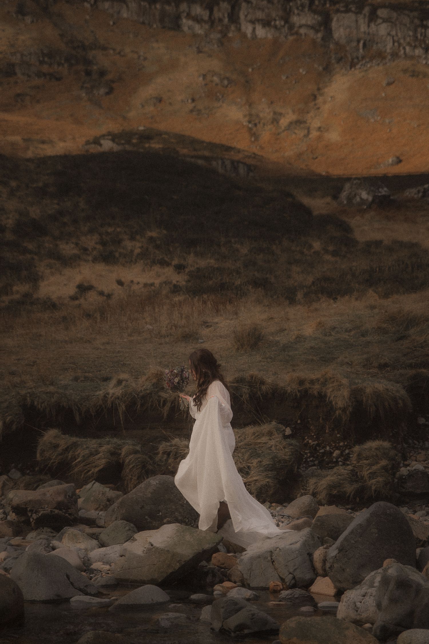 Natural moody photogaphy of a bride climbing across a river during adventure elopement