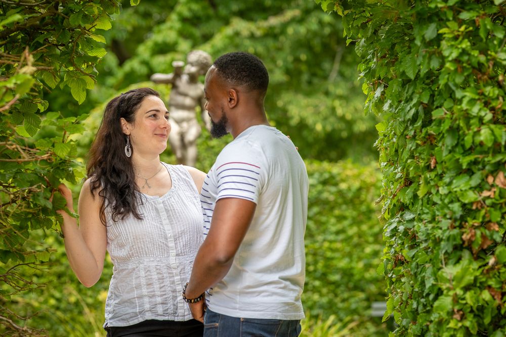 A romantic couple shares a tender moment together while standing amid green foliage in a garden setting.