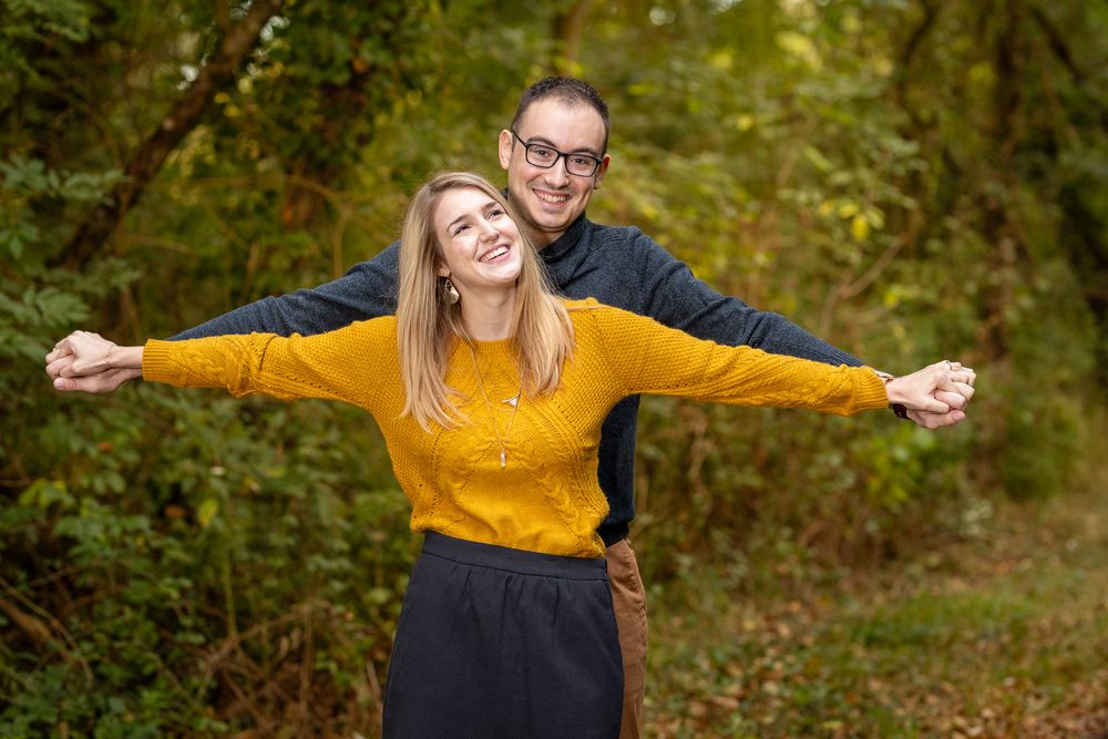 Couple enjoying an autumn walk through a wooded path with golden foliage in the background.