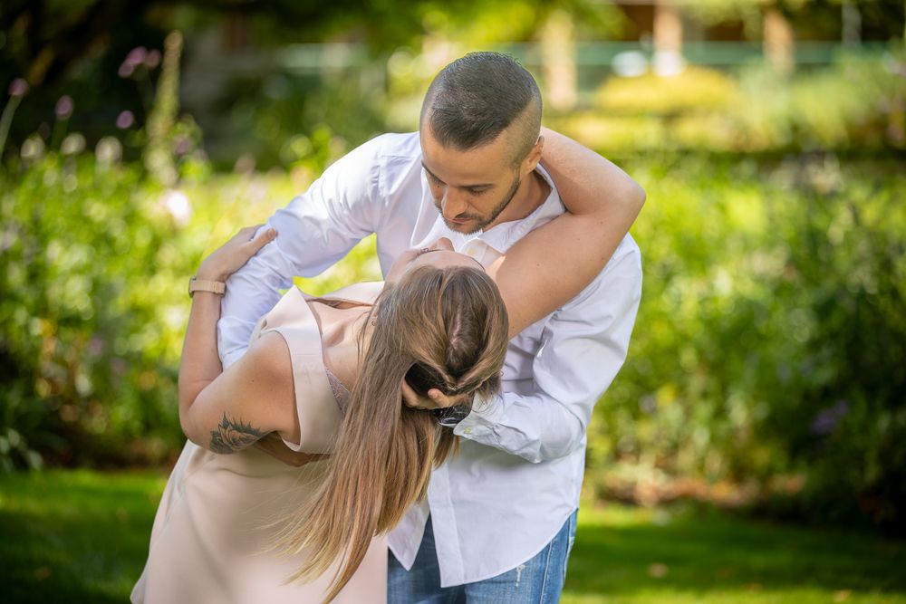 Dancing couple performs romantic dip move outdoors in sunlit garden setting.