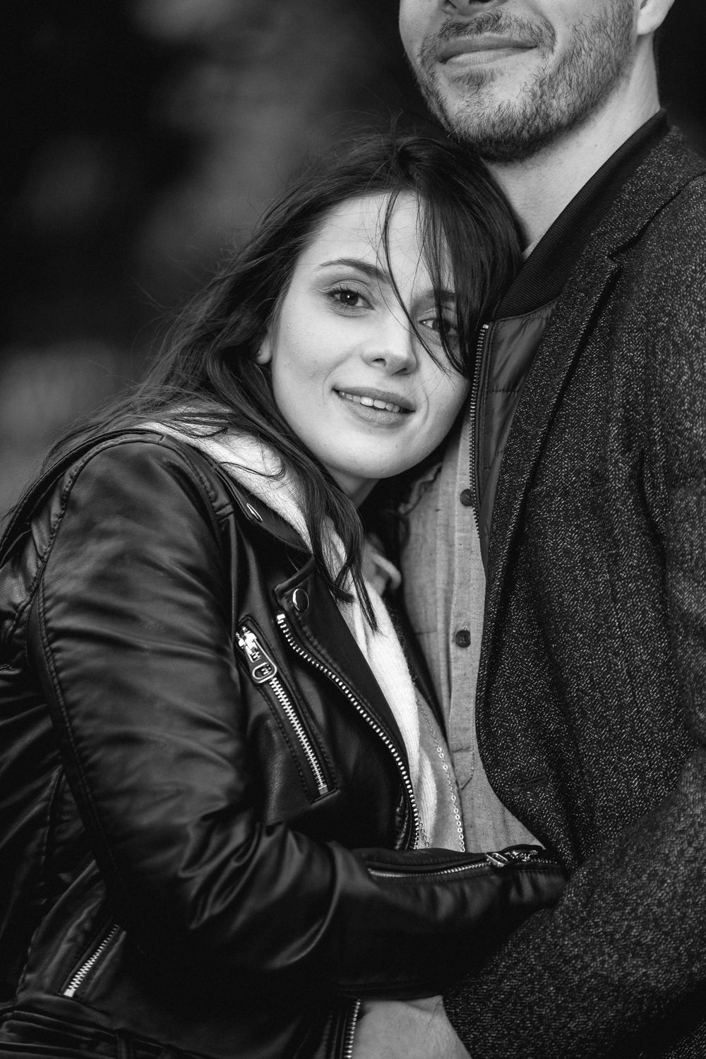 A romantic black and white photo series showing a couple in a leather jacket and sweater embracing and smiling together.