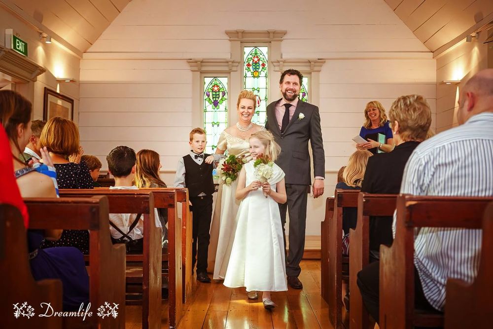 A couple stands at the altar during their wedding ceremony inside a small wooden chapel with stained glass windows.
